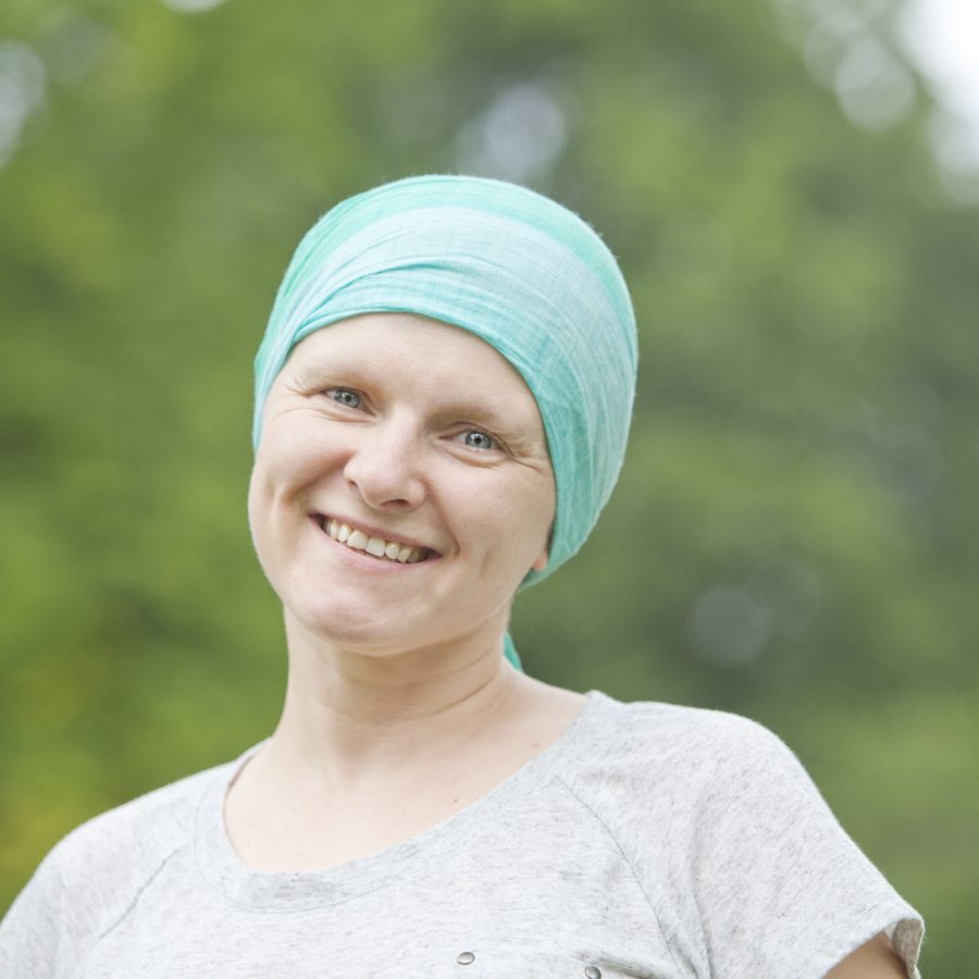 Depiction of woman with the effects of chemotherapy for cancer, smiling outdoors.